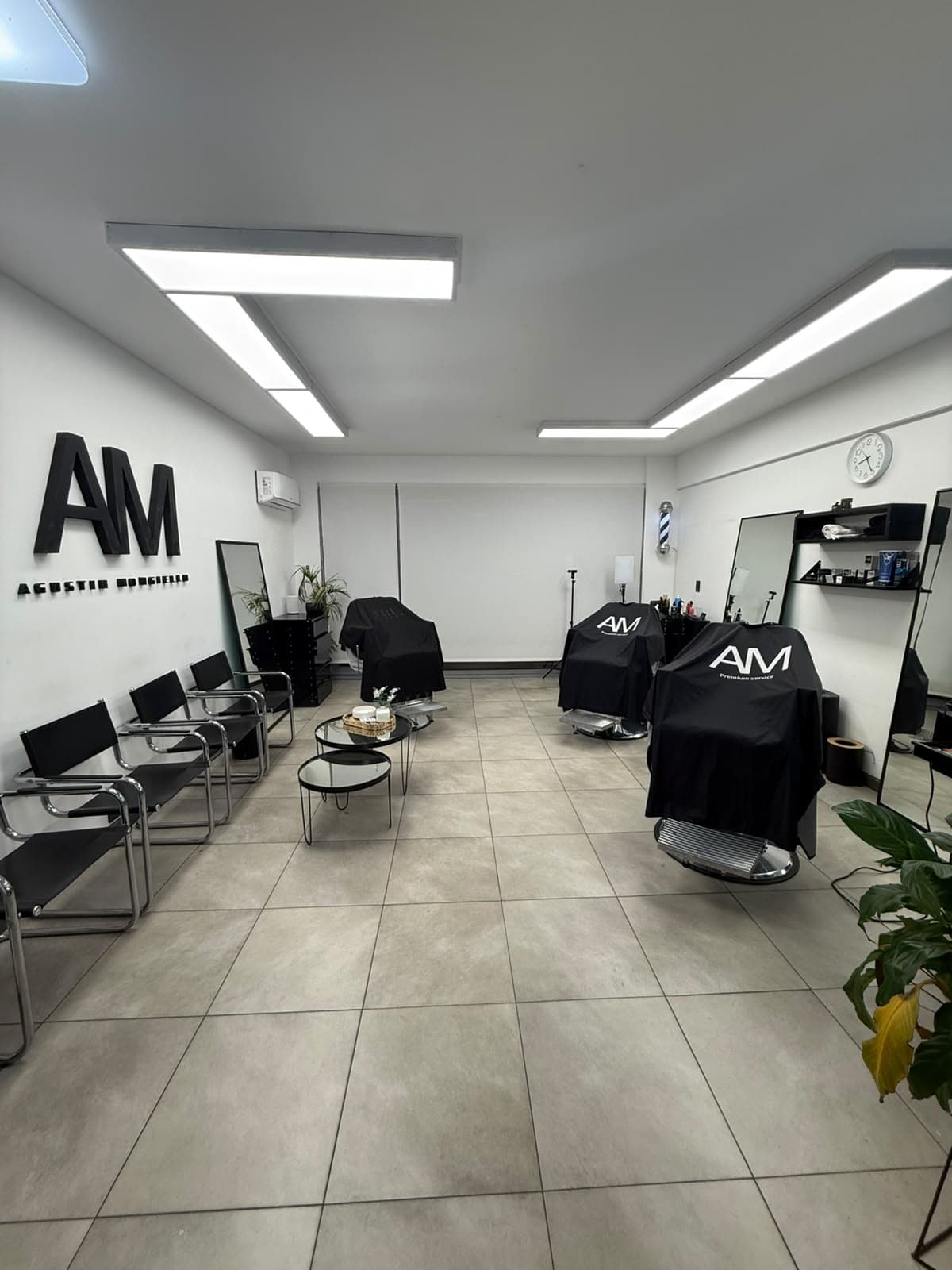Interior de AM Barbería en Villa Urquiza: sala de espera, sillones y logo AM en la pared